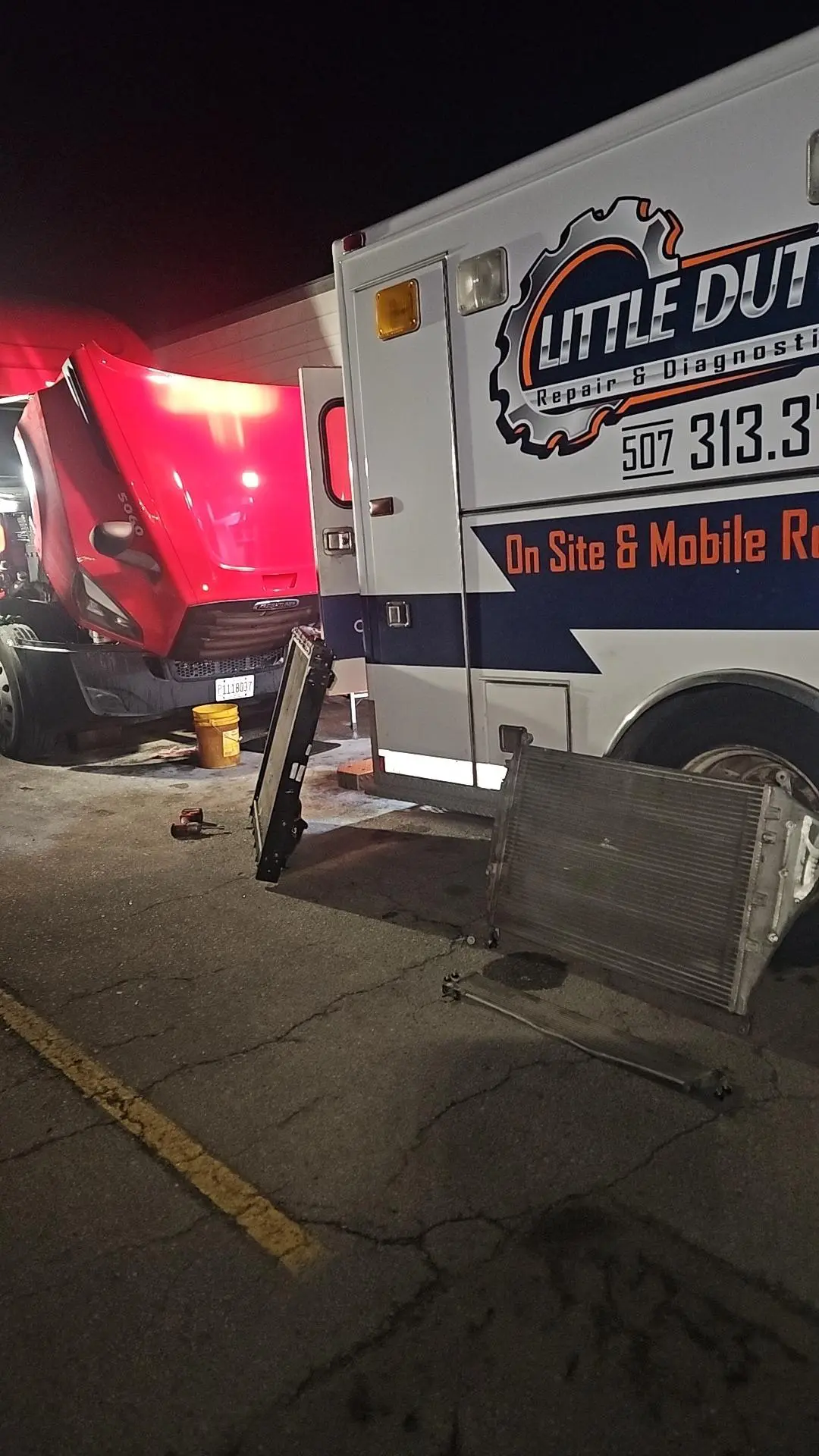 Mobile Little Dutch Repair & Diagnostics service truck parked at night with its logo and phone number visible, a red semi-truck hood open nearby, removed radiator and tools on the pavement showing on-site 24/7 mobile diesel repair and roadside service.