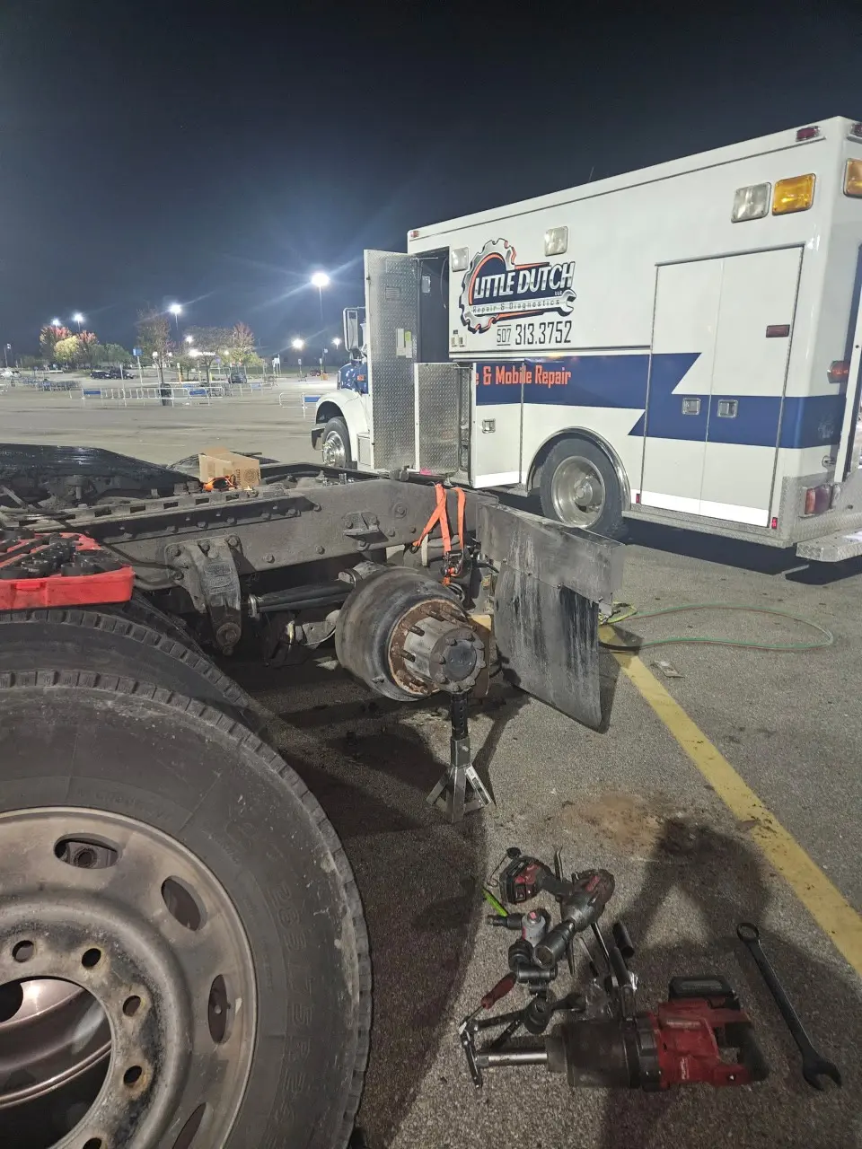 Mobile Little Dutch Repair & Diagnostics emergency service truck at night parked beside a disabled semi with rear axle and drum hub removed, jack stands and tools laid out for 24/7 roadside breakdown and mobile repair.