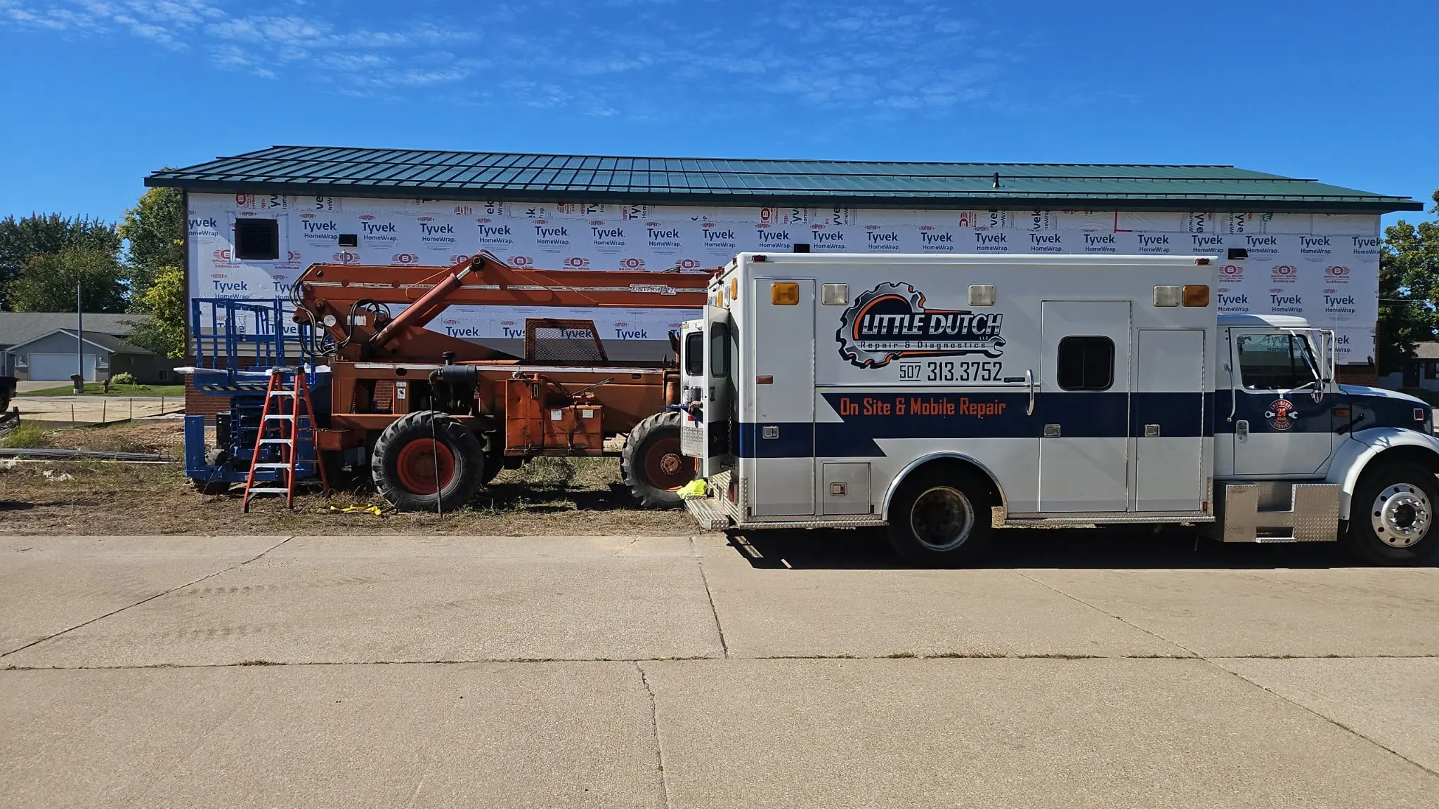 Mobile service truck labeled Little Dutch On Site & Mobile Repair parked next to a construction boom lift in front of a partially wrapped building under a clear blue sky, illustrating 24/7 emergency breakdown and mobile diesel repair services